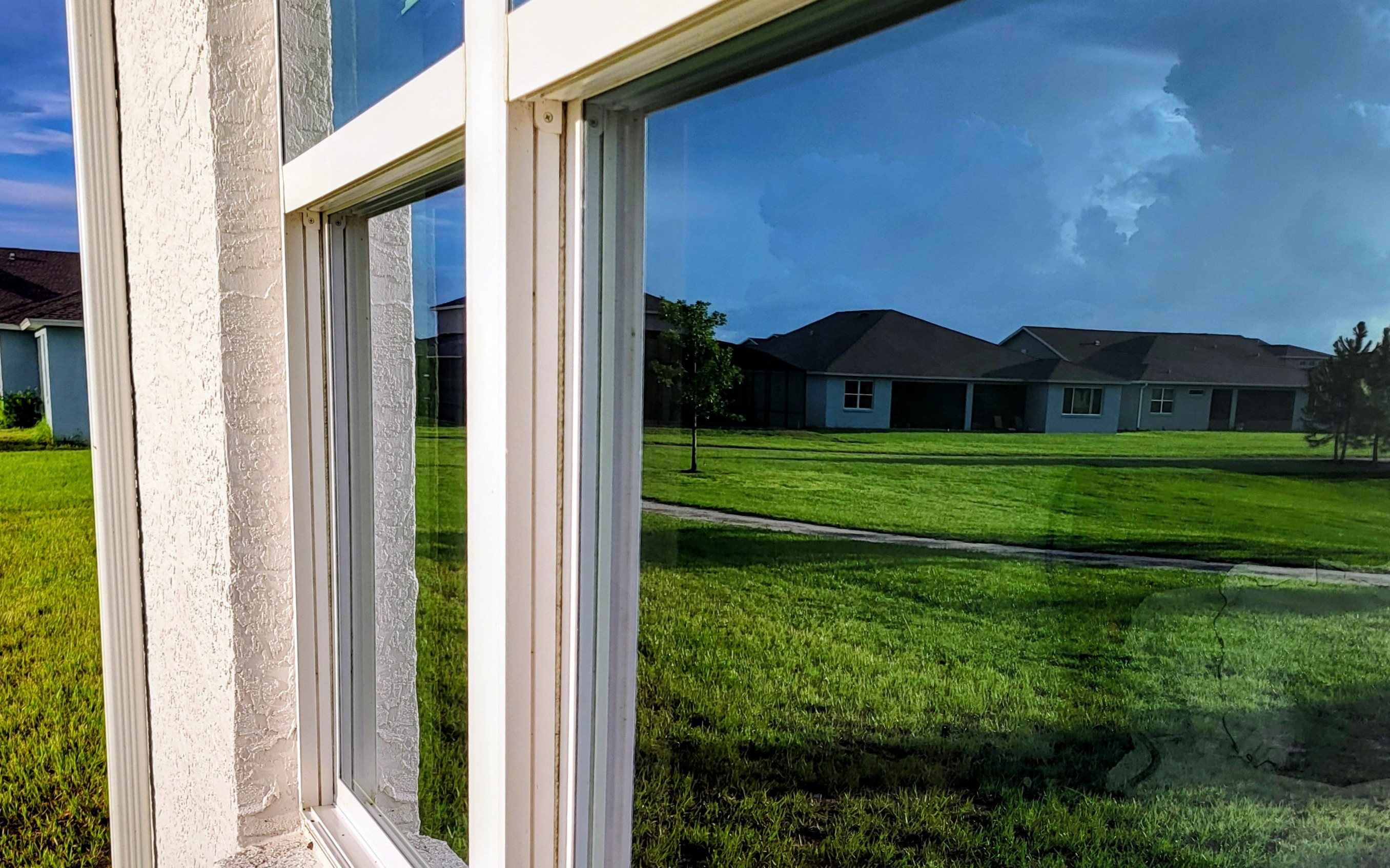 Crystal-clear residential window after H&S Home Services cleaning — white frame and glass reflecting the lawn