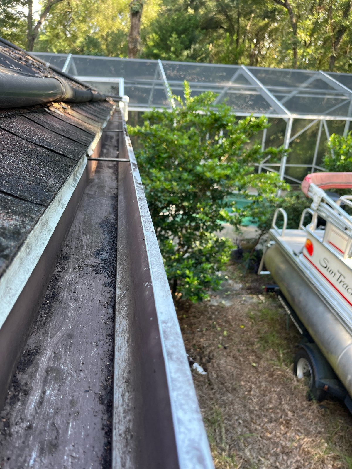 Gutter after — cleared channel above pontoon boat and pool screen enclosure