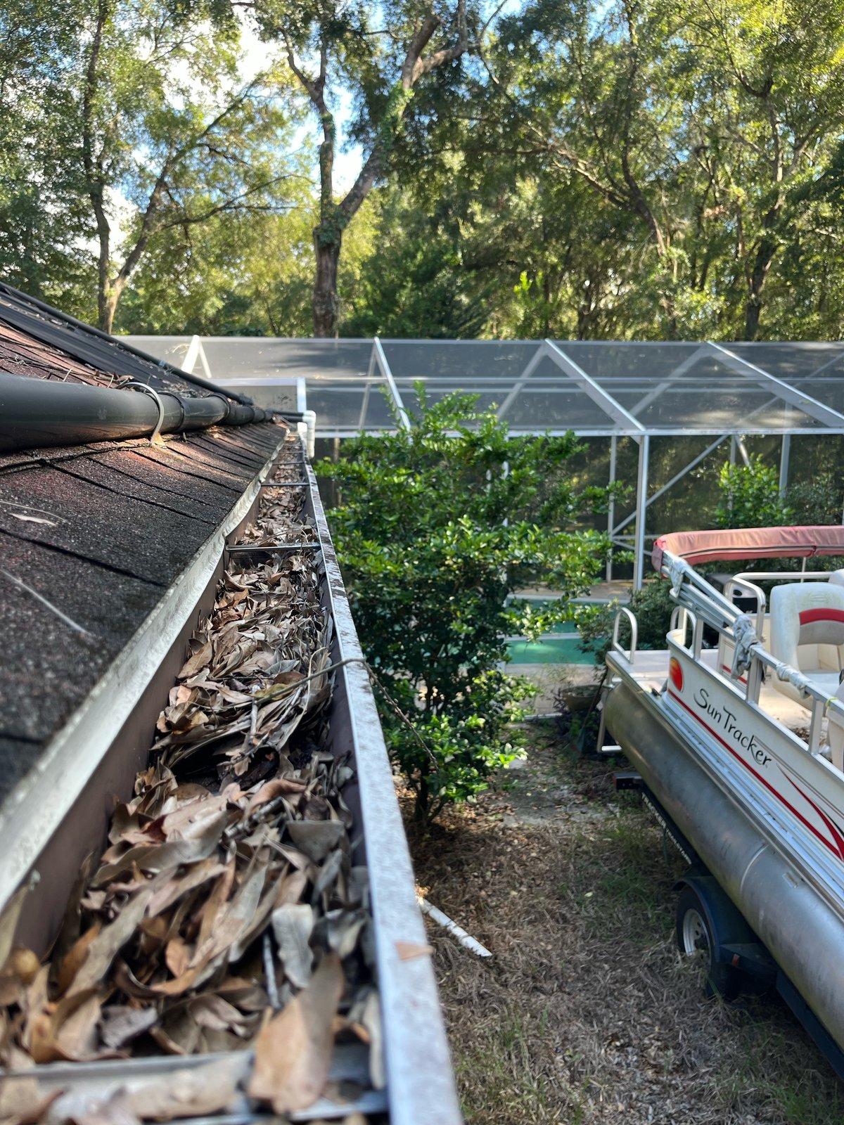 Gutter before — leaf clog above pontoon boat and pool screen enclosure