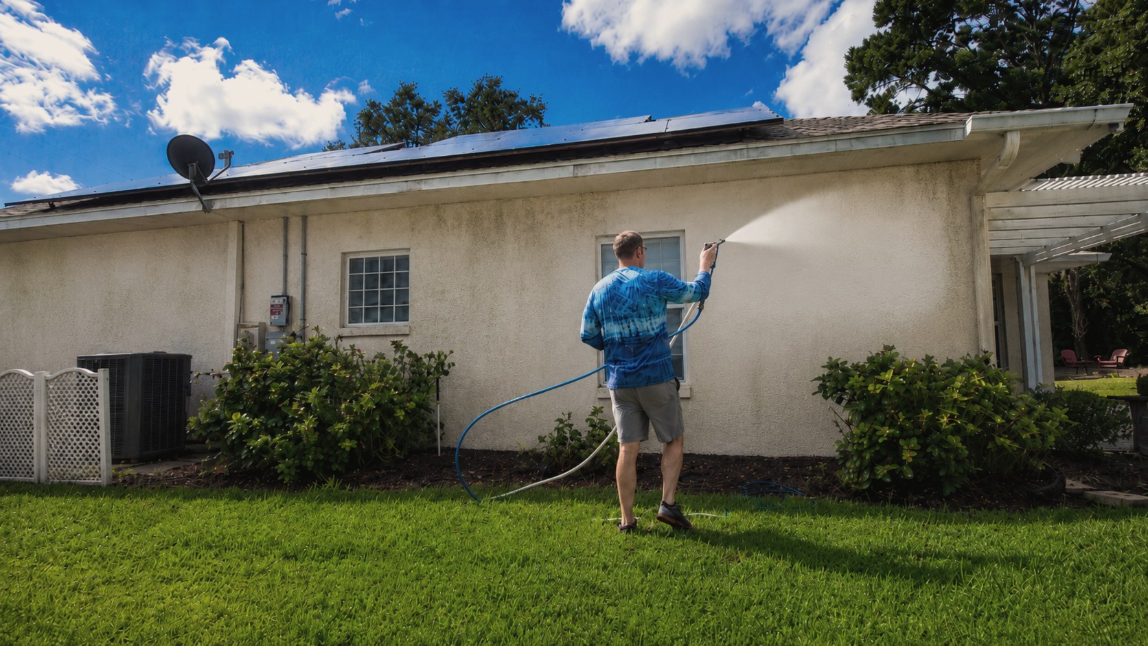 Soft washing a house exterior — spray removing algae and mildew from stucco