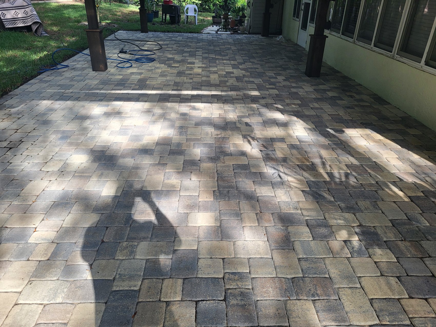 After — cleaned interlocking pavers with light joint sand, blue hose on lawn