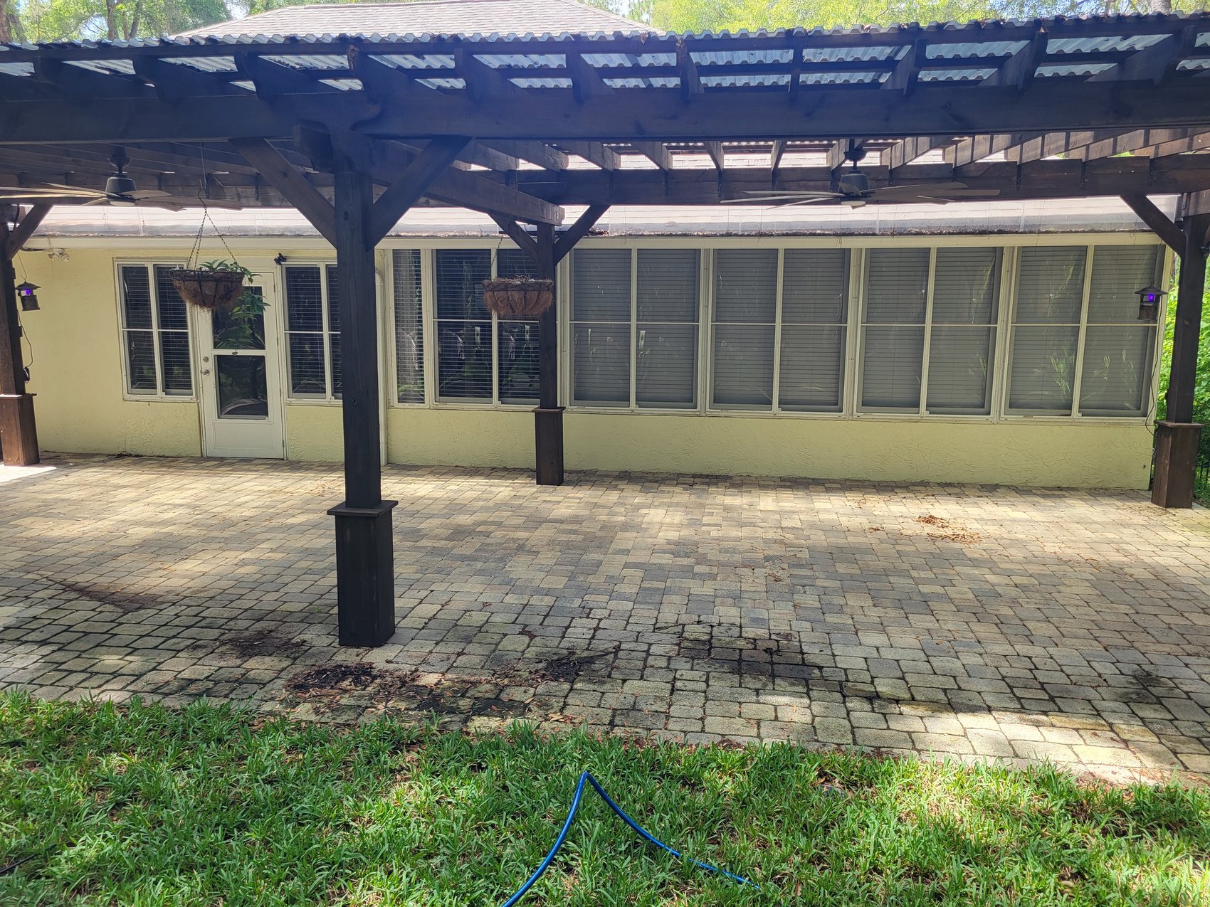 Wide paver patio before — stained pavers under dark wood pergola