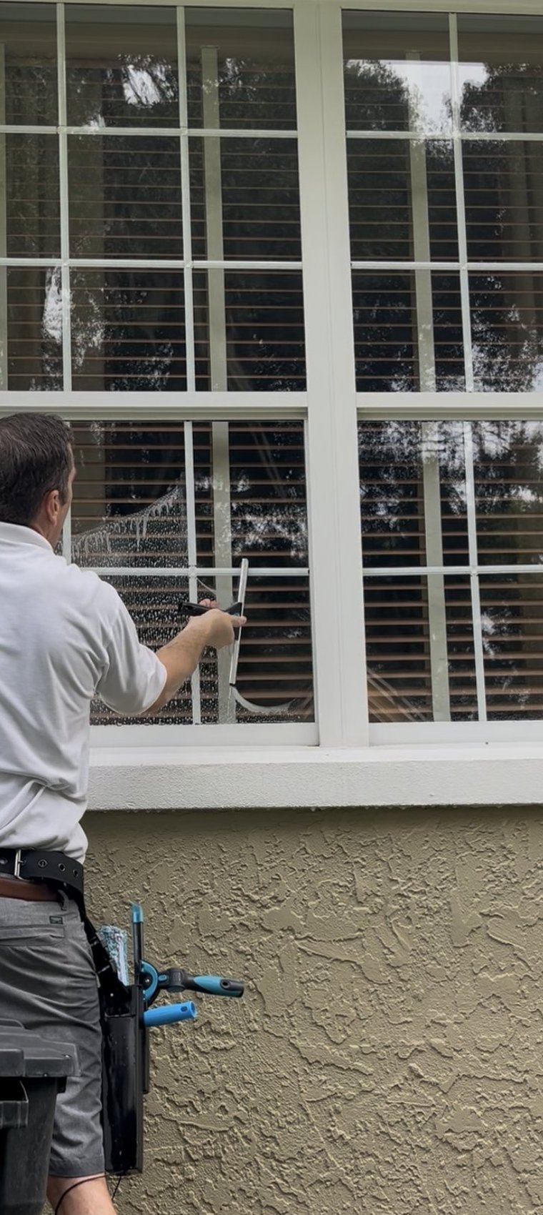 Window cleaning in progress — squeegee on multi-pane glass, tan stucco