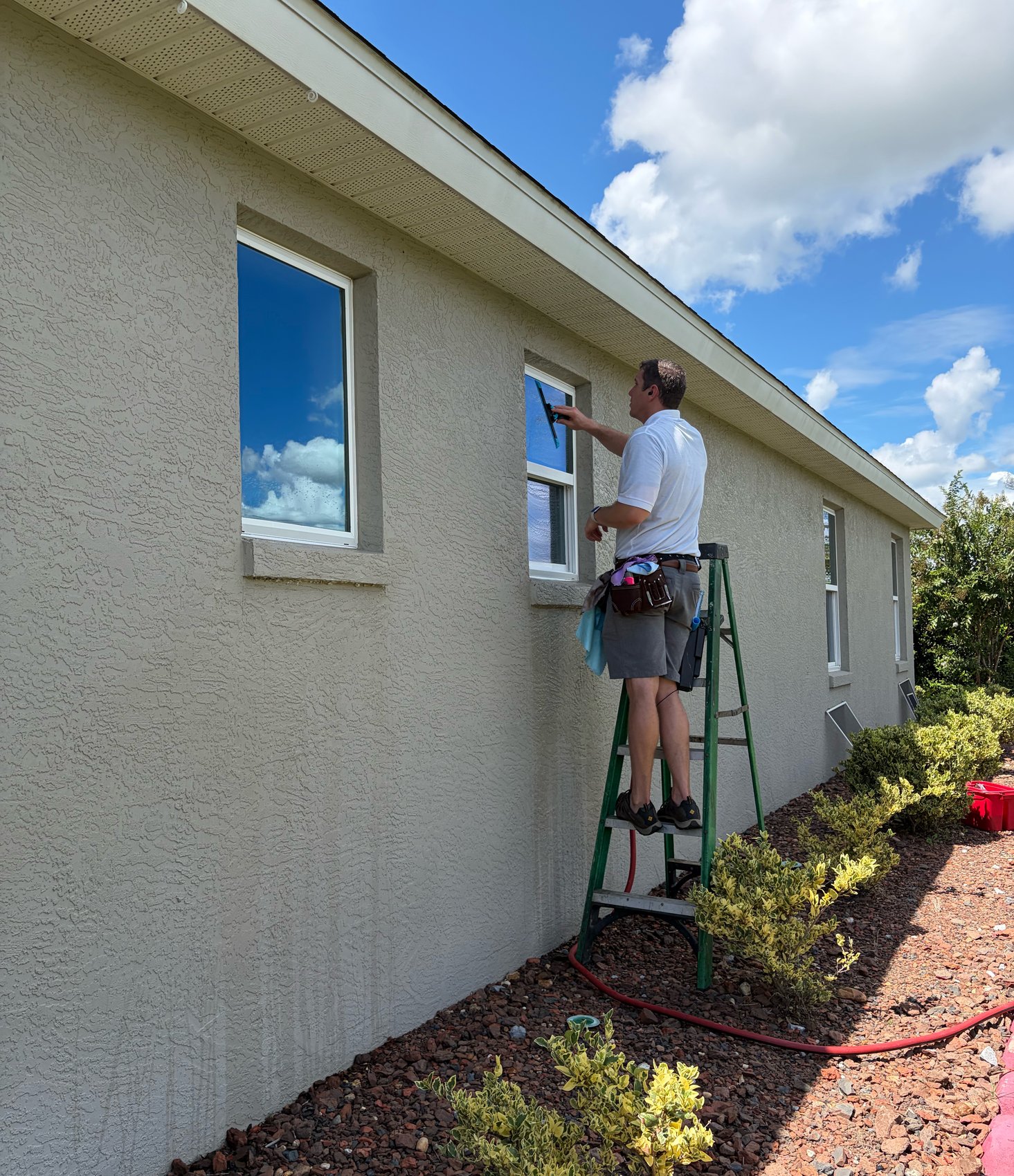 Window cleaning in progress — tech on green ladder at beige stucco windows
