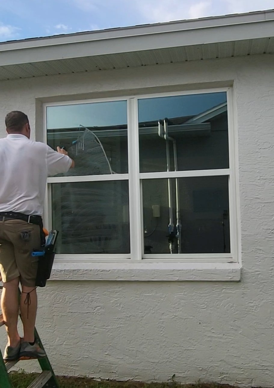 Window cleaning in progress — tech on green ladder squeegeeing glass