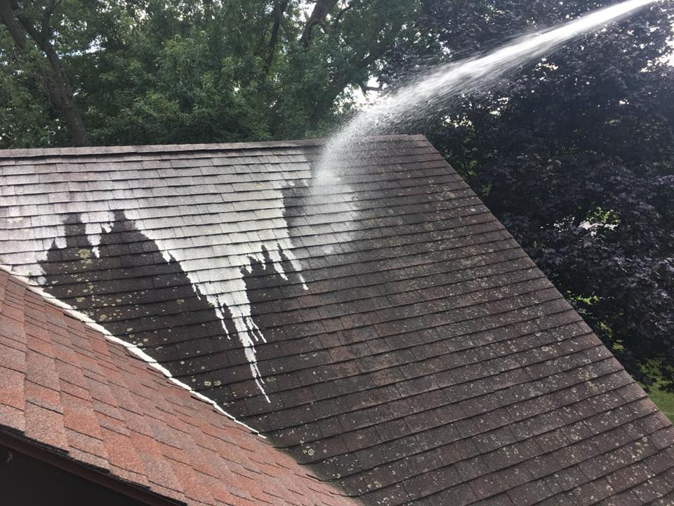 Roof soft wash in progress — spray clearing dark algae from asphalt shingles
